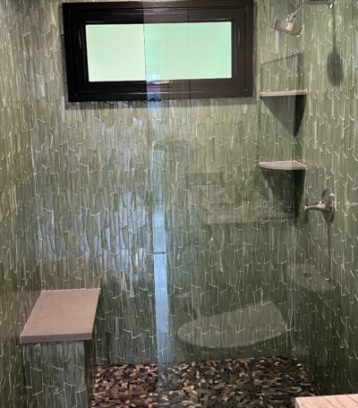 Glass-enclosed green tiled shower with pebble floor